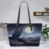 An owl perched on a branch in front of a moonlit landscape leather tote bag