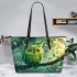 An owl with green feathers perched on the branch of an tree leather tote bag