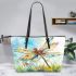 Dragonfly is flying over the grass leather tote bag