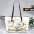 Dragonfly sitting on an open book surrounded flowers leather tote bag