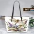 Dragonfly sitting on an open book surrounded flowers leather tote bag