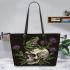 Green frog sitting on top of an skull with purple thistles growing leaather tote bag
