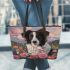Black and white border collie sits in the foreground amidst blooming flowers leather tote bag