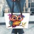 Cute colorful owl with big eyes sitting on a tree branch leather tote bag