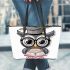 Grey owl with big eyes wearing glasses and graduation hat holding leather tote bag