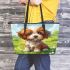 Cute brown and white puppy is sitting on the grass leather tote bag