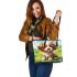 Cute brown and white puppy is sitting on the grass leather tote bag