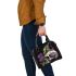 Green frog sitting on top of an skull with purple thistles growing shoulder handbag