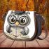 Grey owl with big eyes wearing glasses and graduation hat holding saddle bag